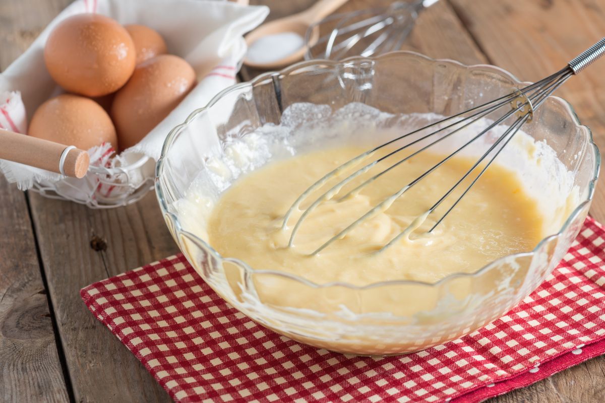 Ciotola di vetro con impasto torta mescolato con frusta da cucina