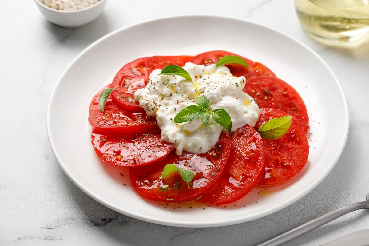 Insalata di pomodori condita con sale, pepe e basilico accompagnata da stracciatella