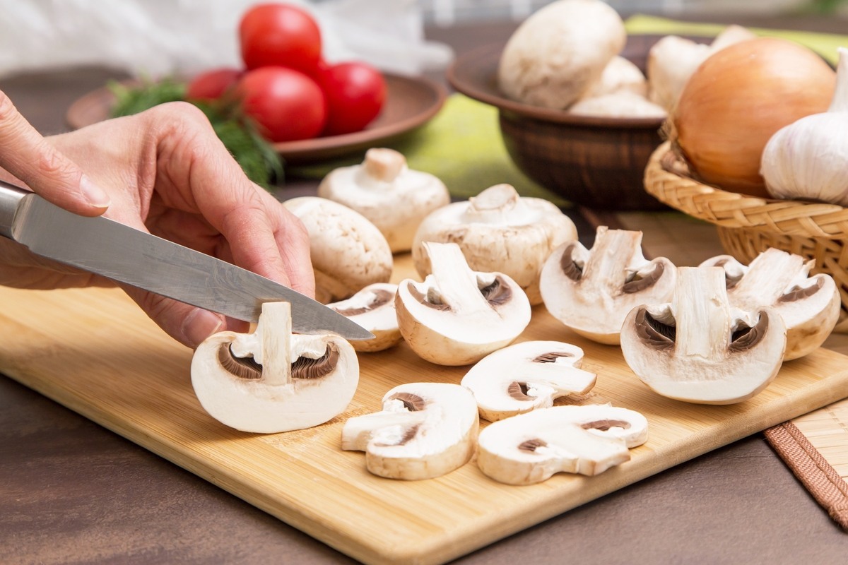 Mani di donna che tagliano funghi champignon su tagliere di legno