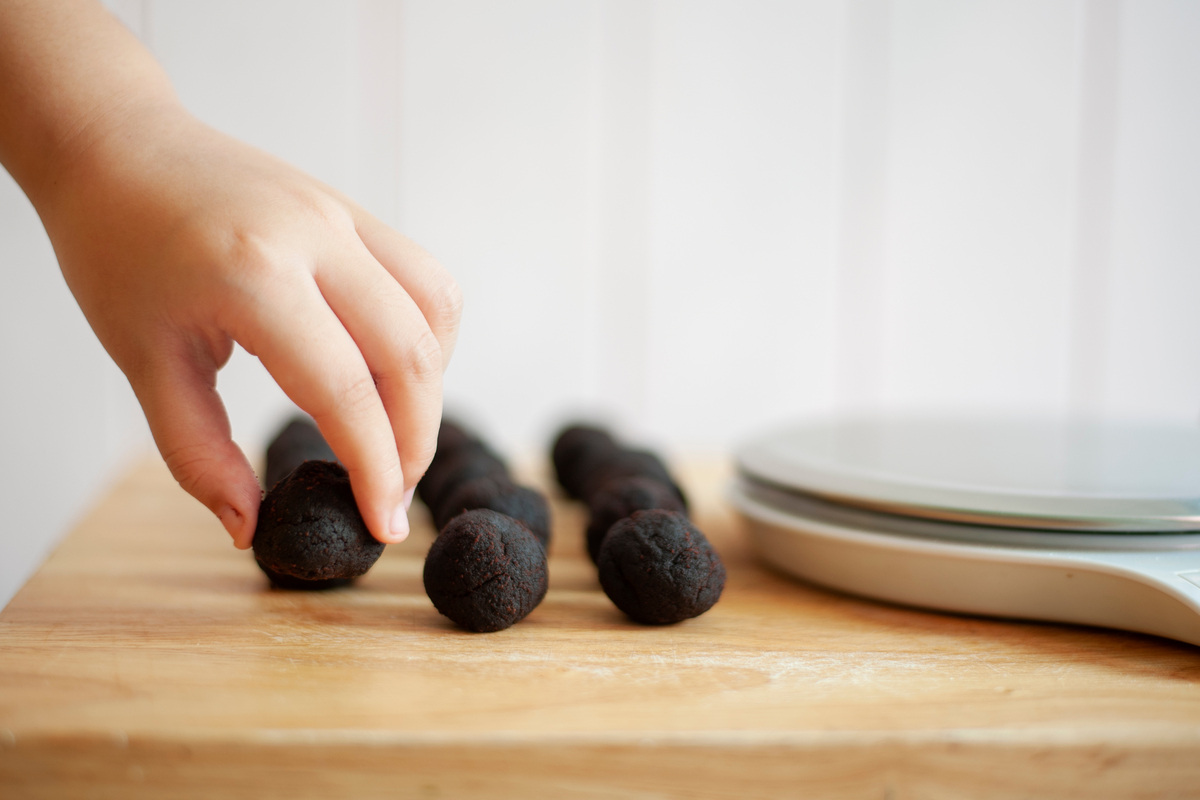 Mani che allineano cake pop al cioccolato su tagliere di legno