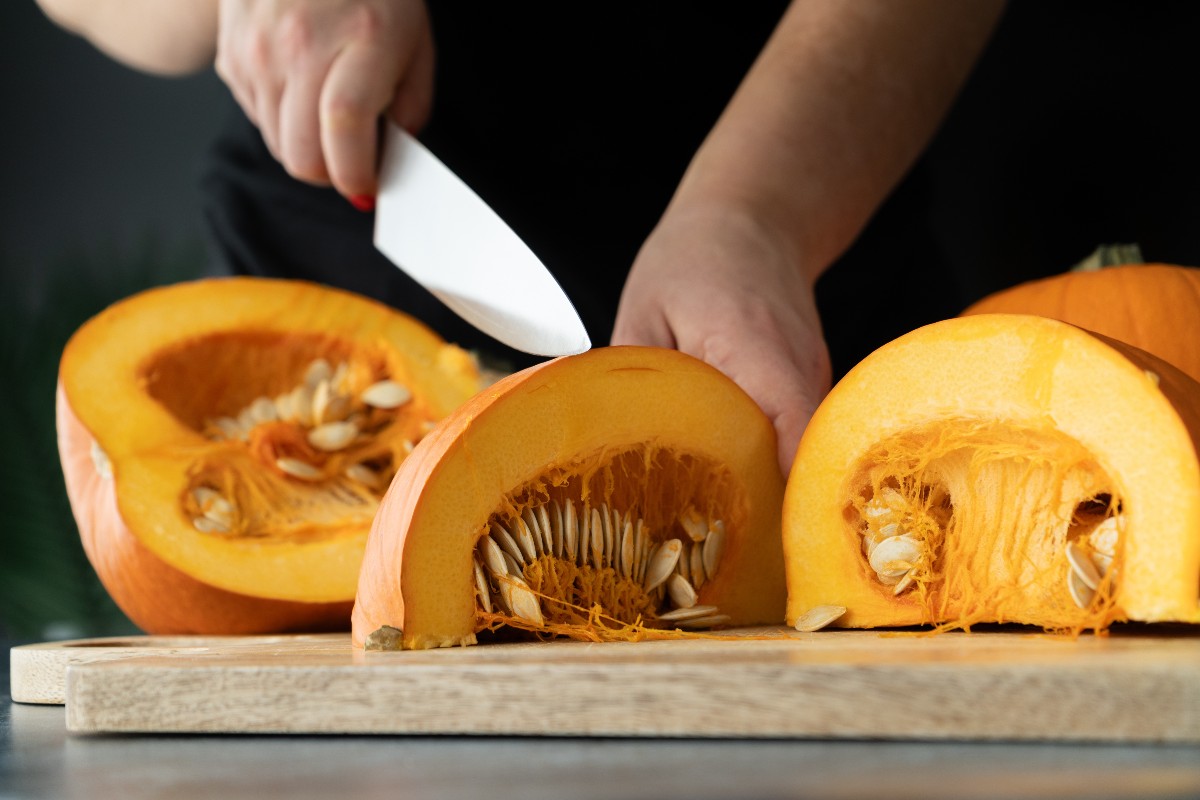 Mani che tagliano zucca su tagliere di legno