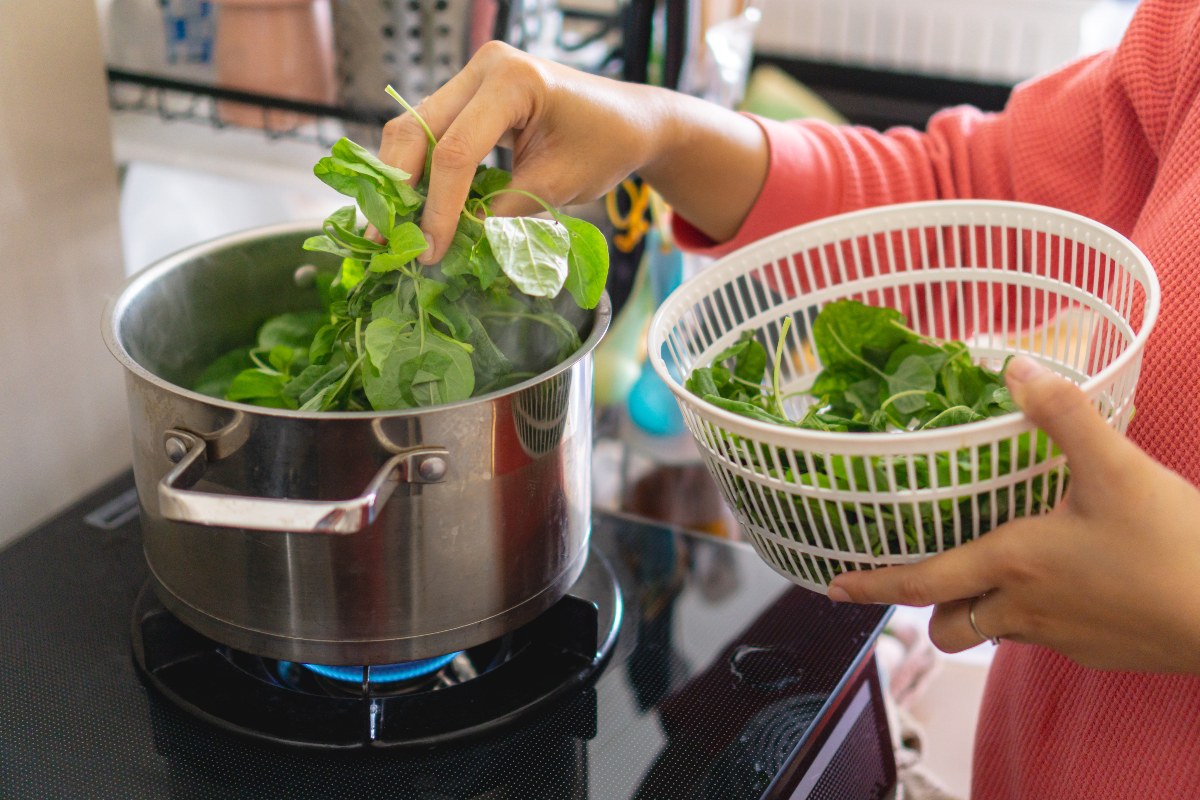 Mano di donna che tuffa gli spinaci in acqua bollente