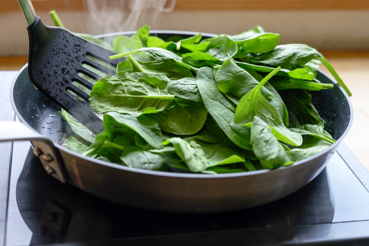 Spinaci a crudo in padella  mescolati con paletta da cucina 