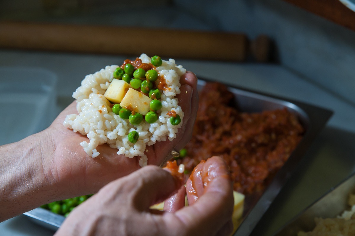 Preparazione arancini con riso allargato sulla mano e sopra ragù con piselli e formaggio