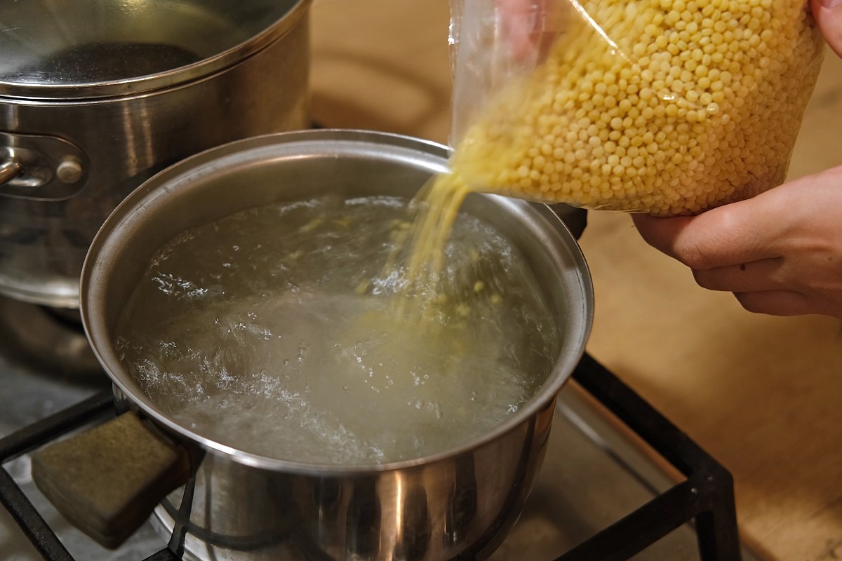 Mani che versano fregola in pentola di acqua a bollore