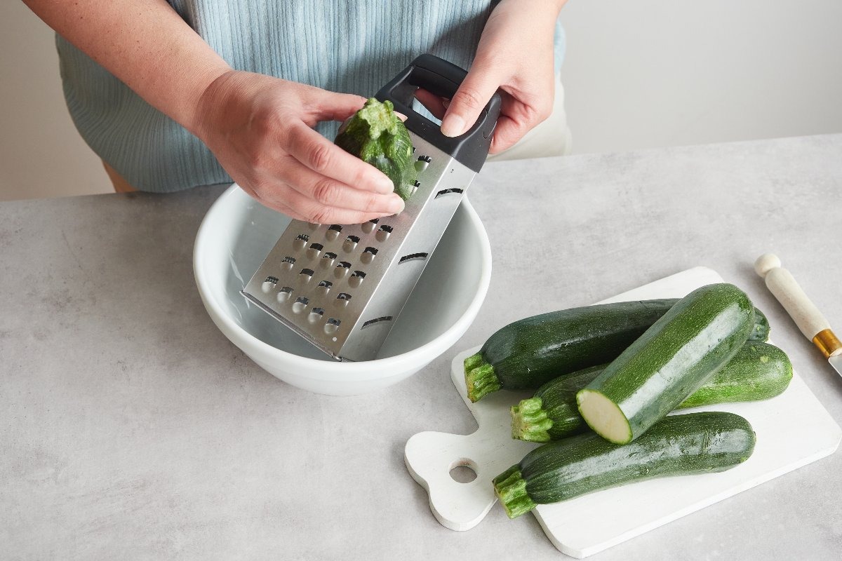 Mani di donna che grattugiano le zucchine con grattugia a fori grossi
