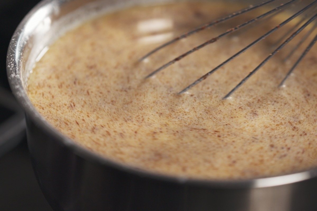 Pentola con composto per budino alla cannella mescolato con frusta da cucina