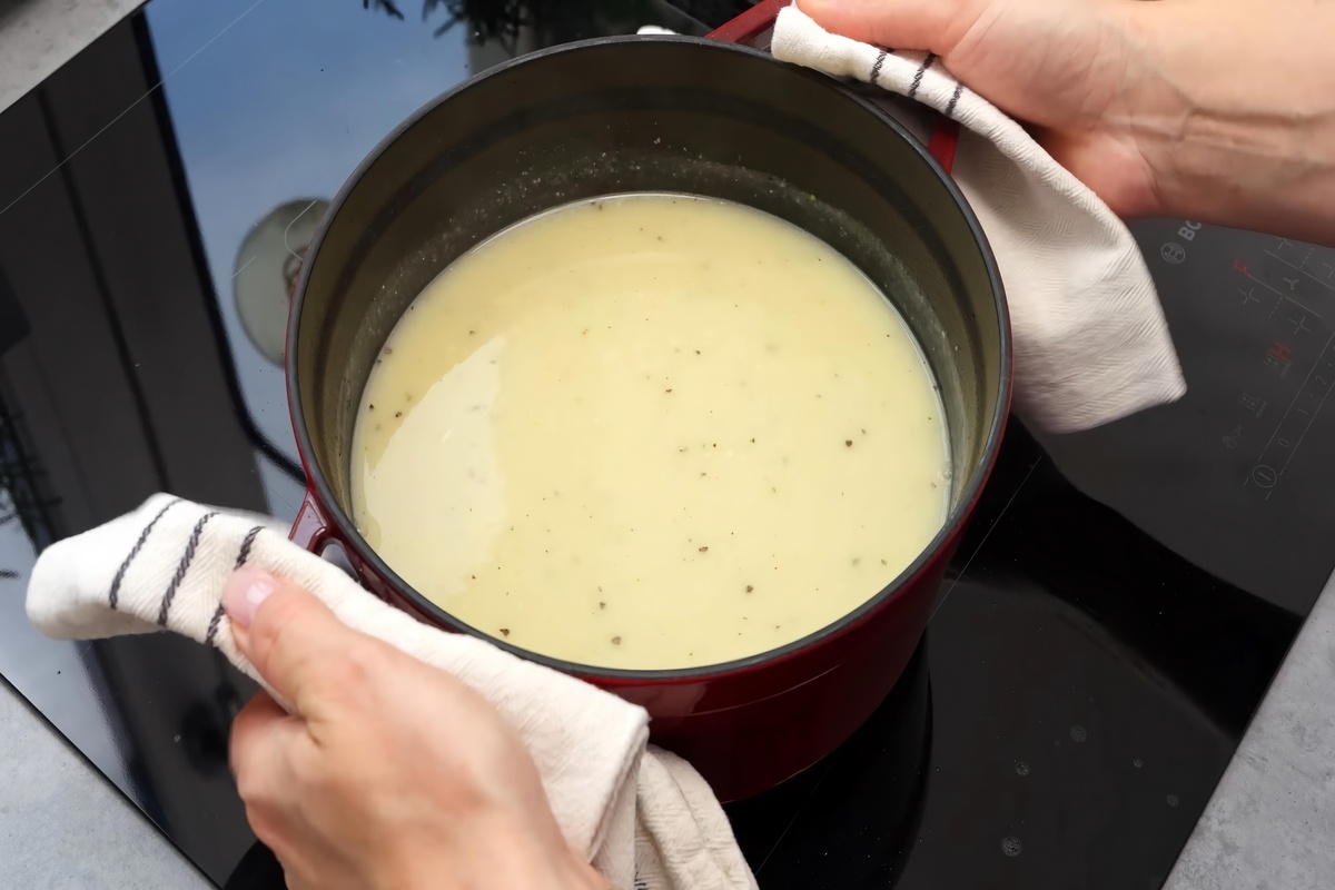 Mani di donna che tolgono dal fuoco una pentola con la zuppa