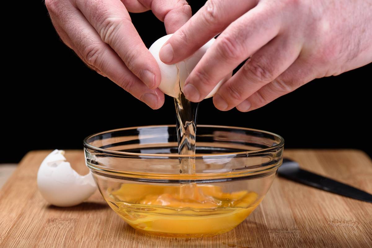 Mani maschili che rompono le uova in una ciotola di vetro