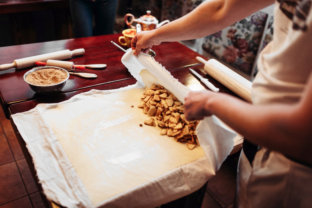 Mani di donna che preparano lo strudel avvolgendo la pasta strudel sulle mele
