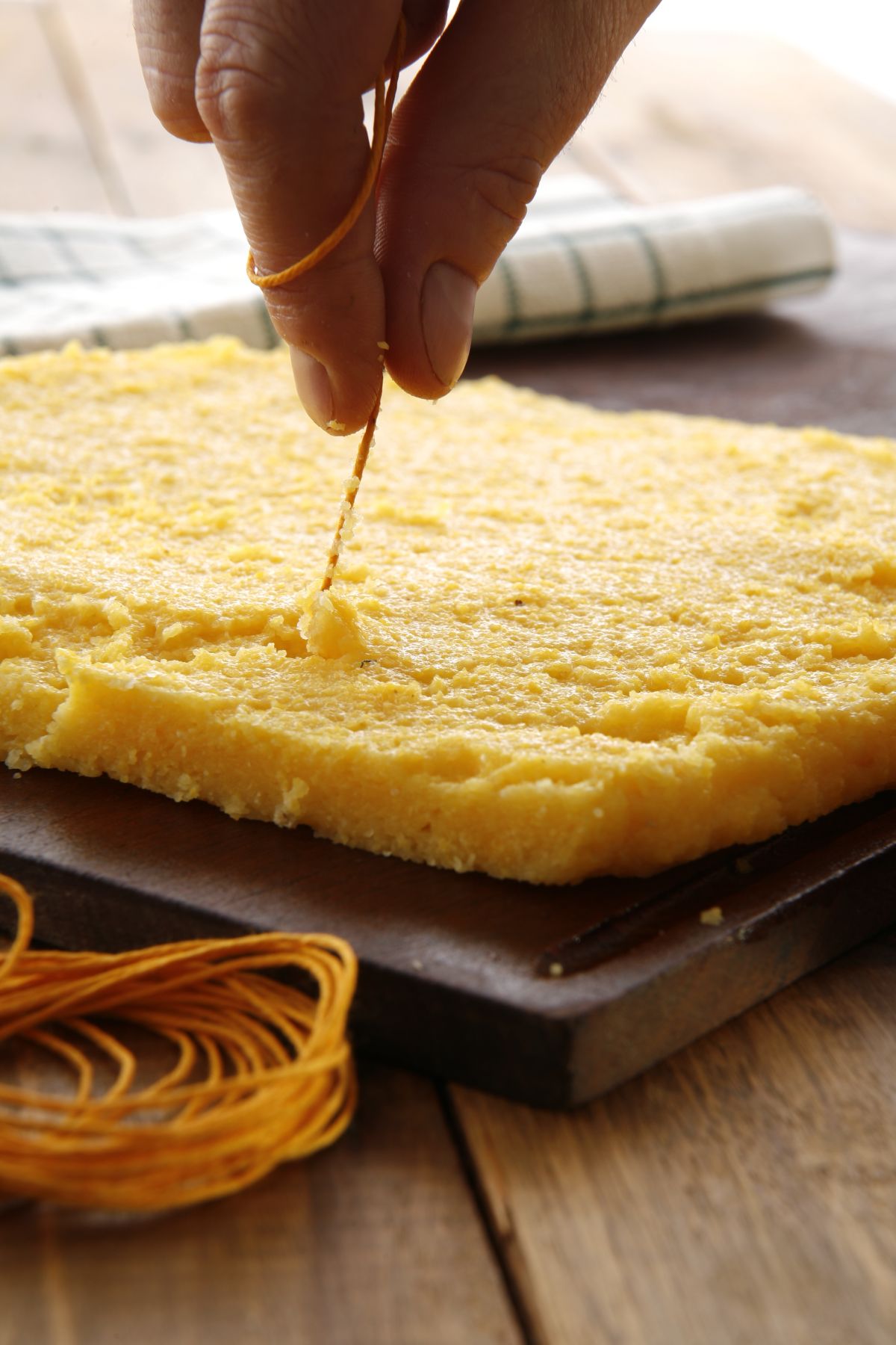 Mani che tagliano polenta stesa solidificata aiutandosi con un filo