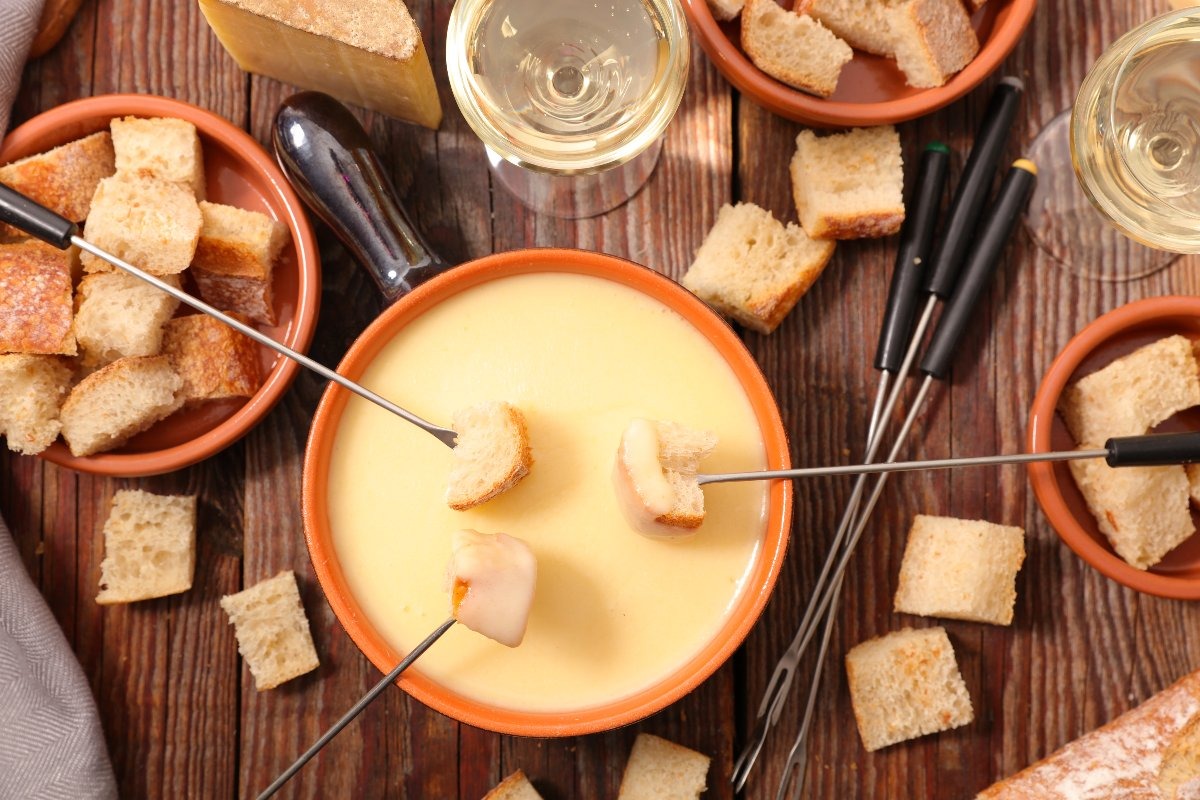 Vista dall'alto ciotola di terracotta con fonduta di formaggi in cui viene intinto pane con apposite forchettine