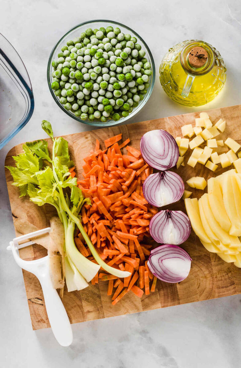Vista dall'alto di sedano, carota, cipolla, patate e piselli su tagliere di legno