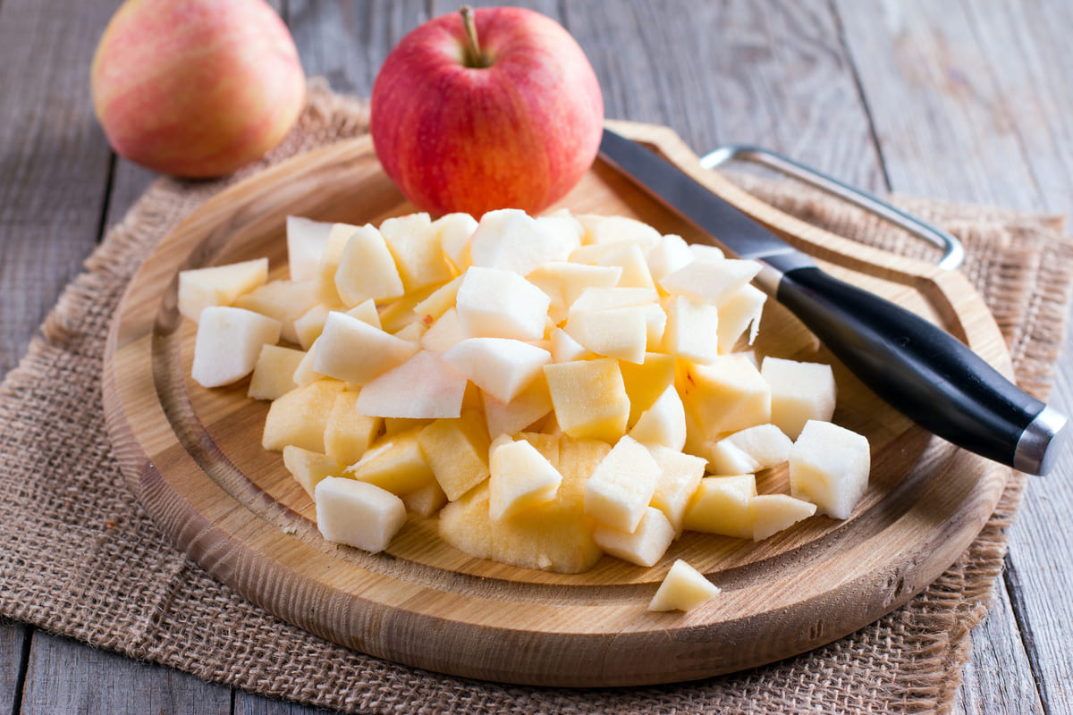 Tagliere di legno con mele tagliate a dadini e frutti interi sullo sfondo