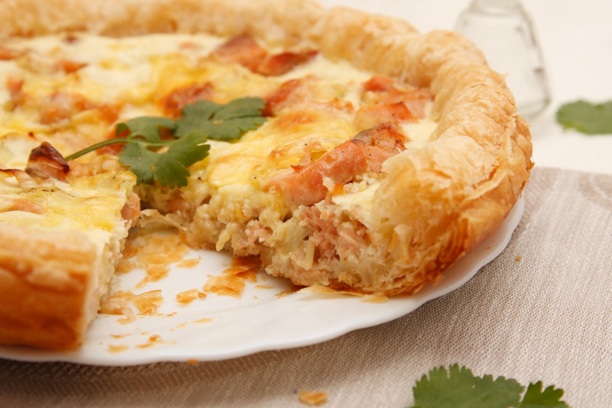 Torta salata con salmone a cui manca una fetta su un piatto bianco 