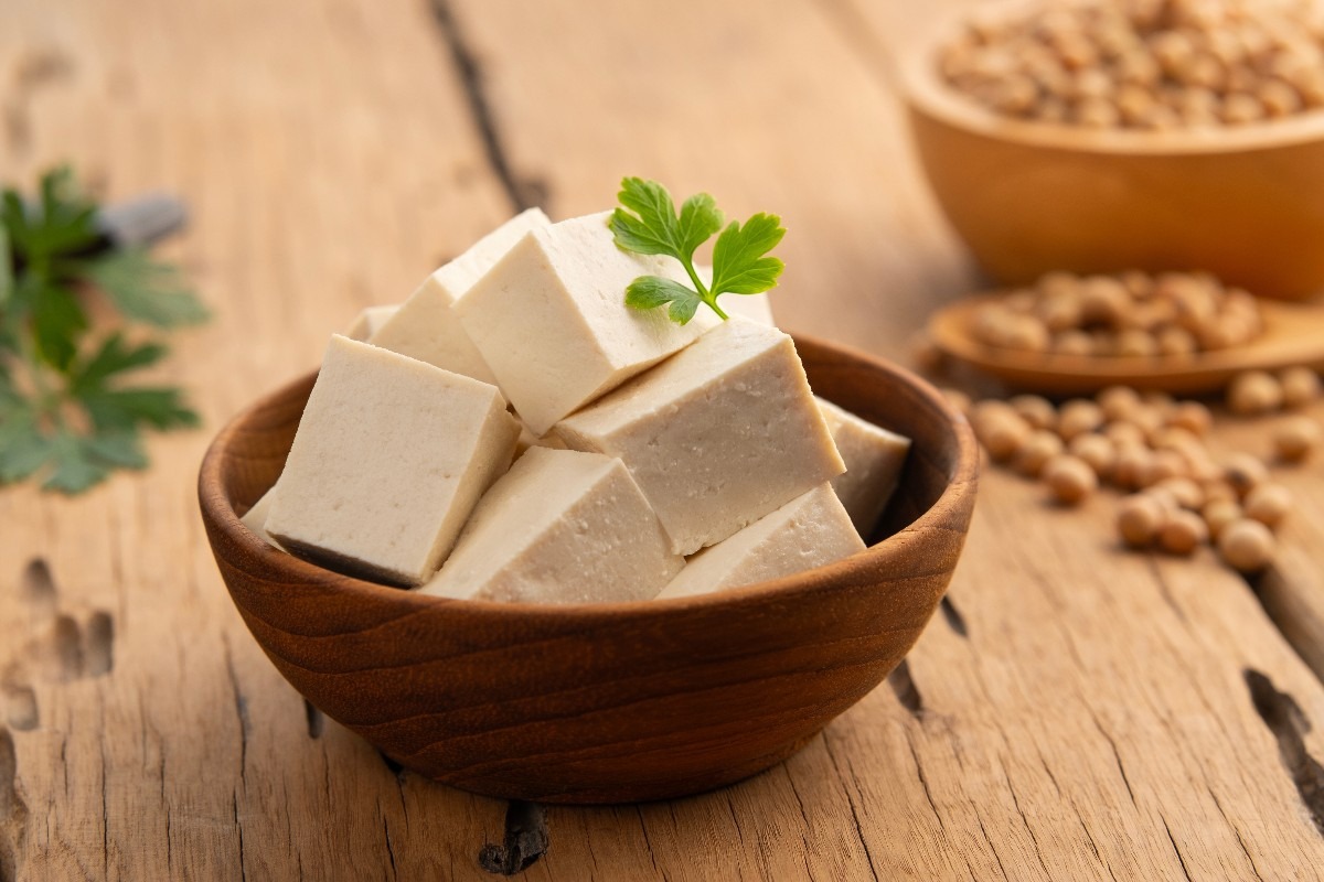 Ciotola di bambù con tofu a cubetti e fagioli di soia sullo sfondo