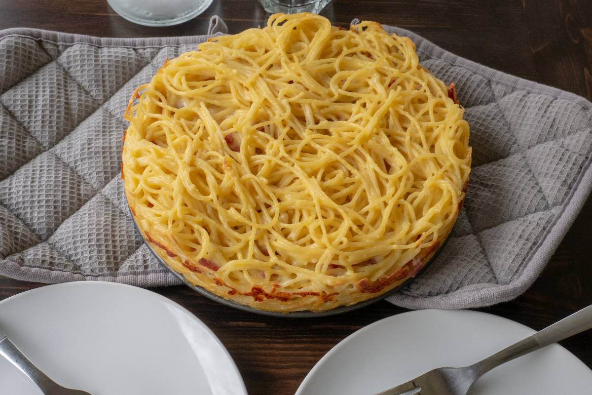 Frittata di spaghetti cotta in padella posata su due presine