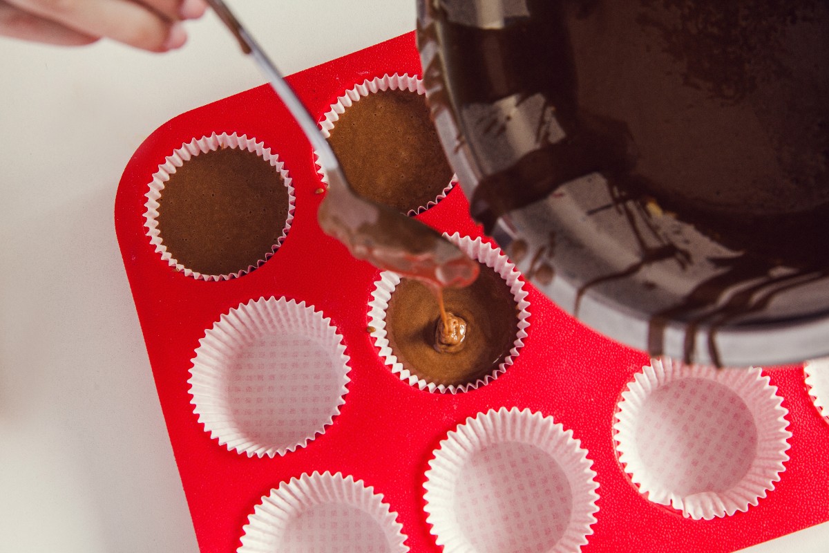 Vista dall'alto impasto muffin al cioccolato versato negli stampi con cucchiaio 