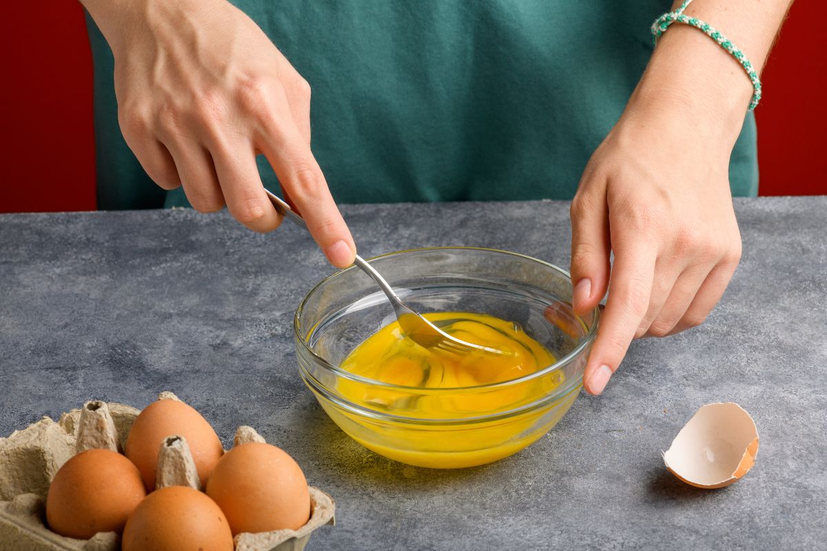 Mani di donna che mescolano uova in una ciotola per preparare la frittata