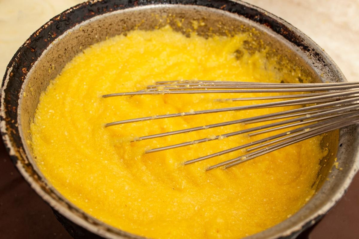 Paiolo con polenta in cottura e frusta da cucina per mescolarla