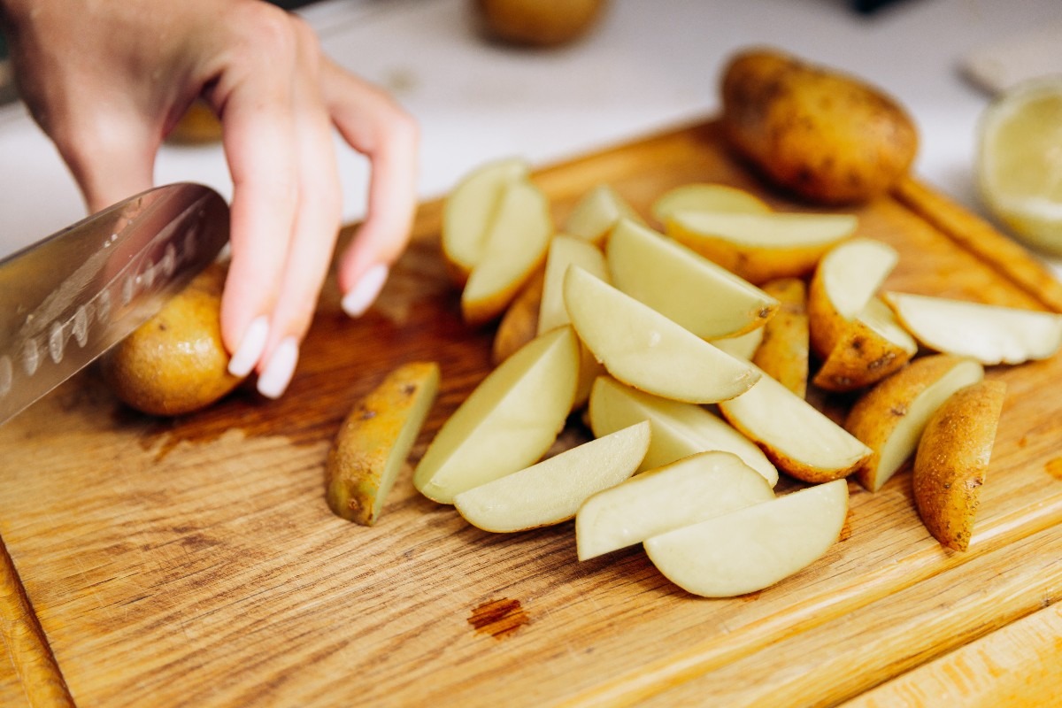 Mani di donna che tagliano patate a spicchi su tagliere di legno