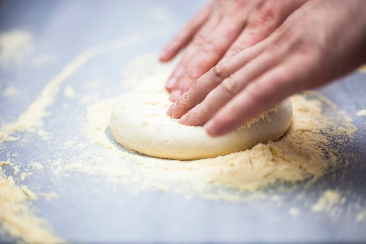 Mani che stendono impasto pizza su spianatoia infarinata