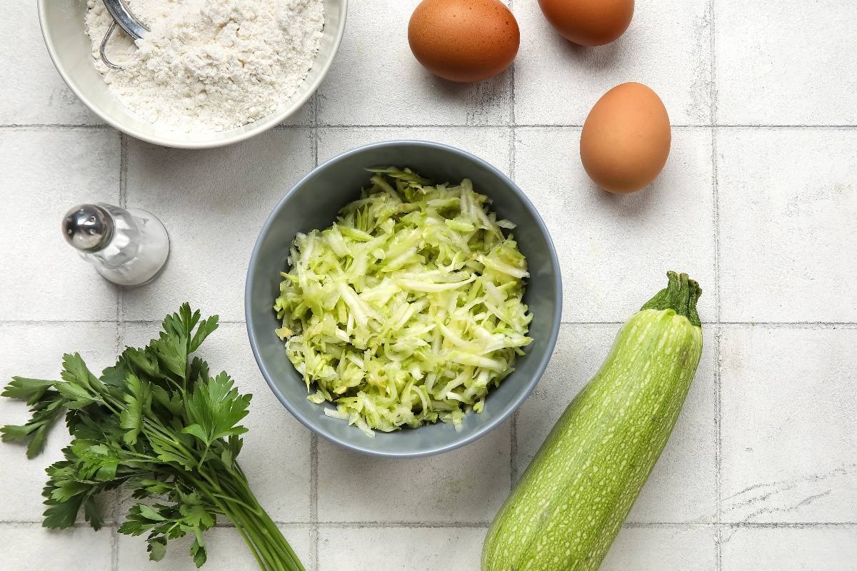 Vista dall'alto ciotola con zucchine grattugiate, prezzemolo, farina, sale e uova