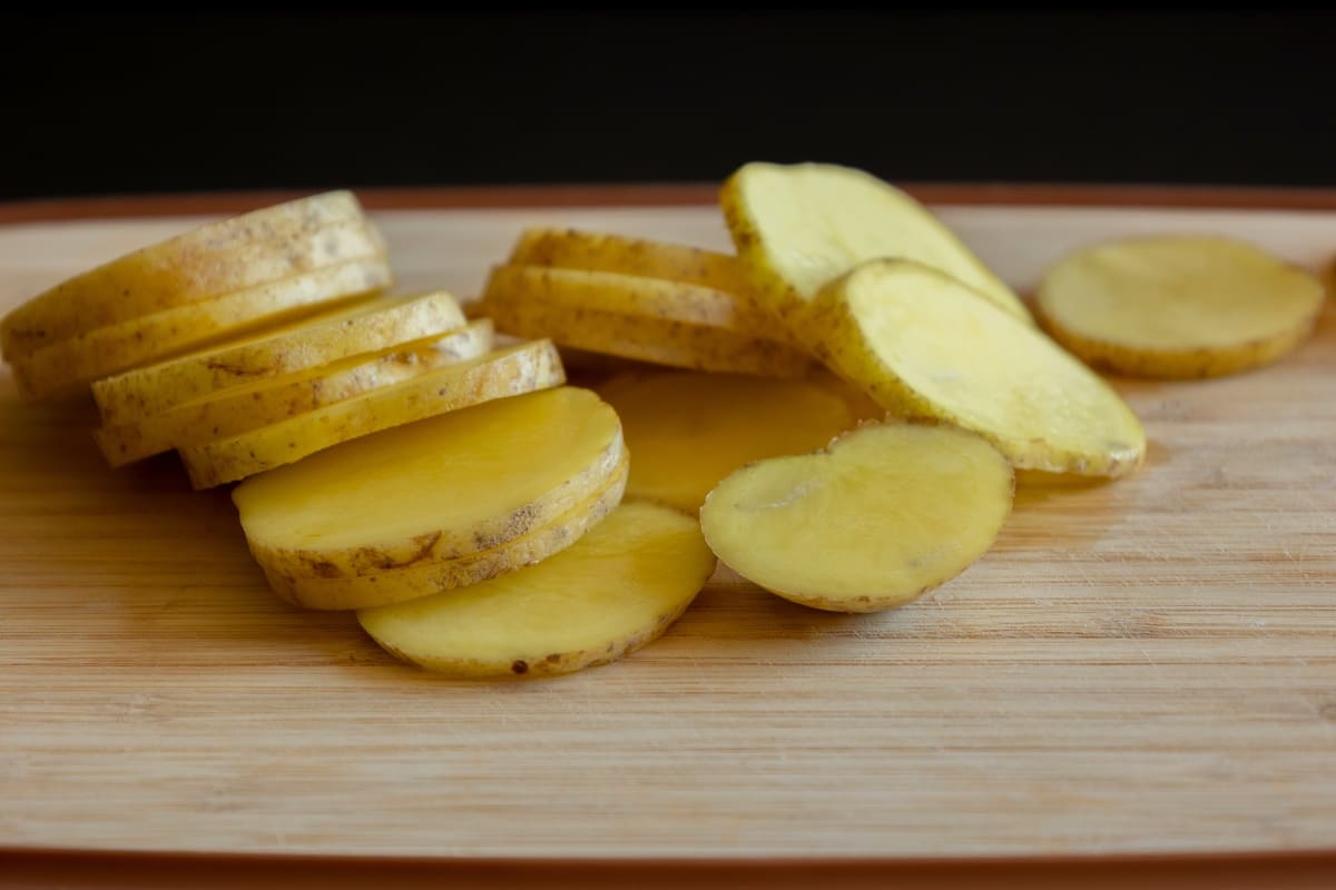 Patate tagliate a fette con la buccia su tagliere di legno