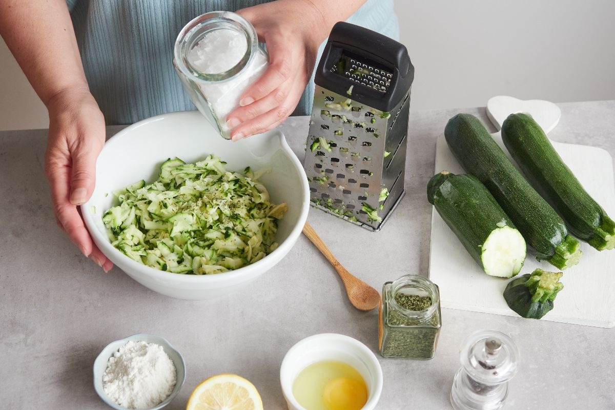 Preparazione sformato di zucchine con zucchine grattugiate in ciotola e attorno altri ingredienti