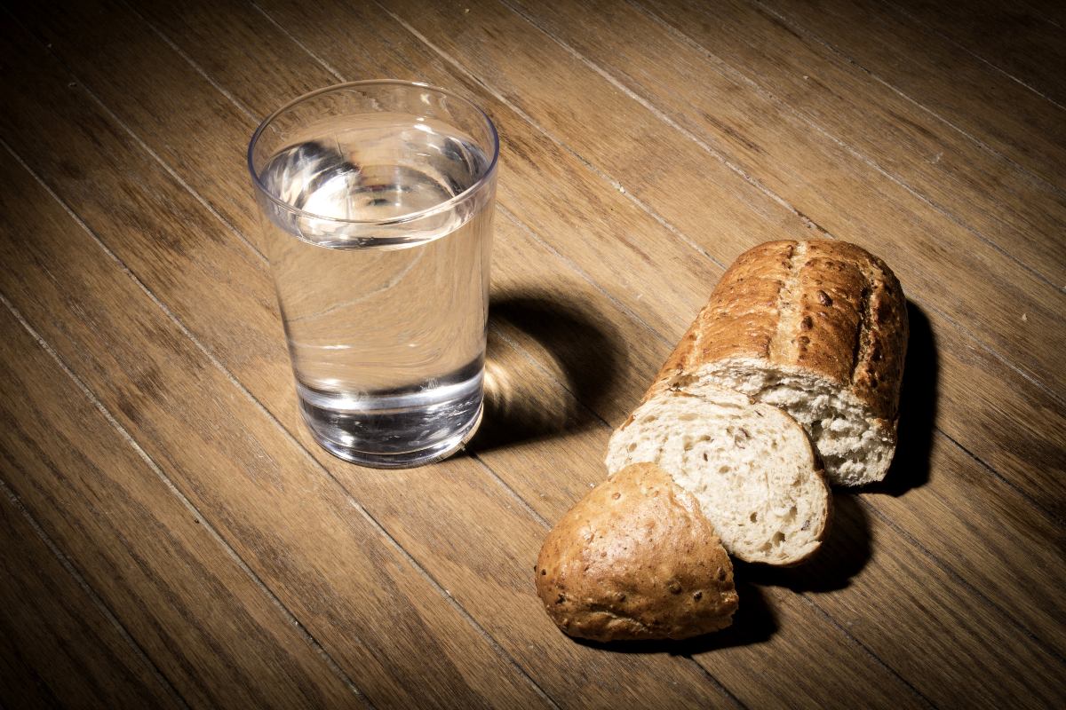 Un bicchiere d'acqua e del pane affettato appoggiati sopra un piano di legno.