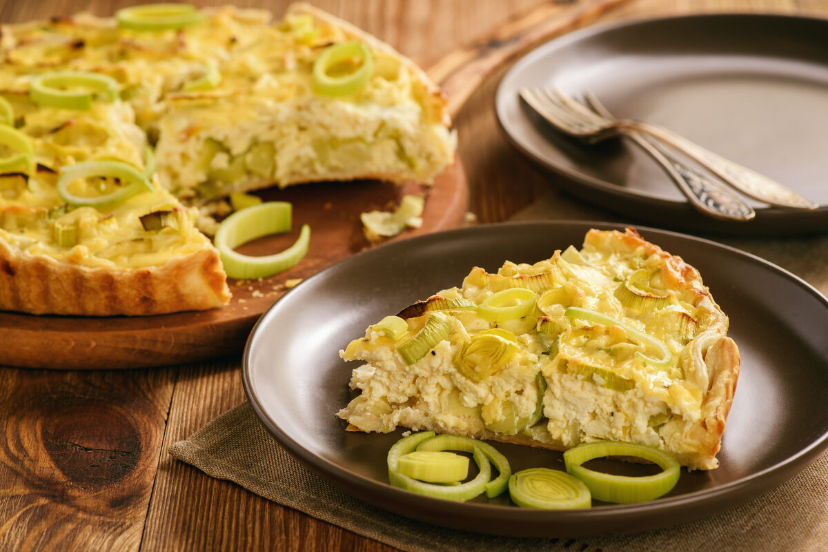 Fetta di torta salata ai porri su piatto con torta salata intera sullo sfondo