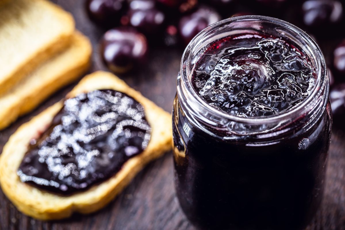 Vasetto di marmellata di uva con vicino fetta biscottata spalmata di marmellata