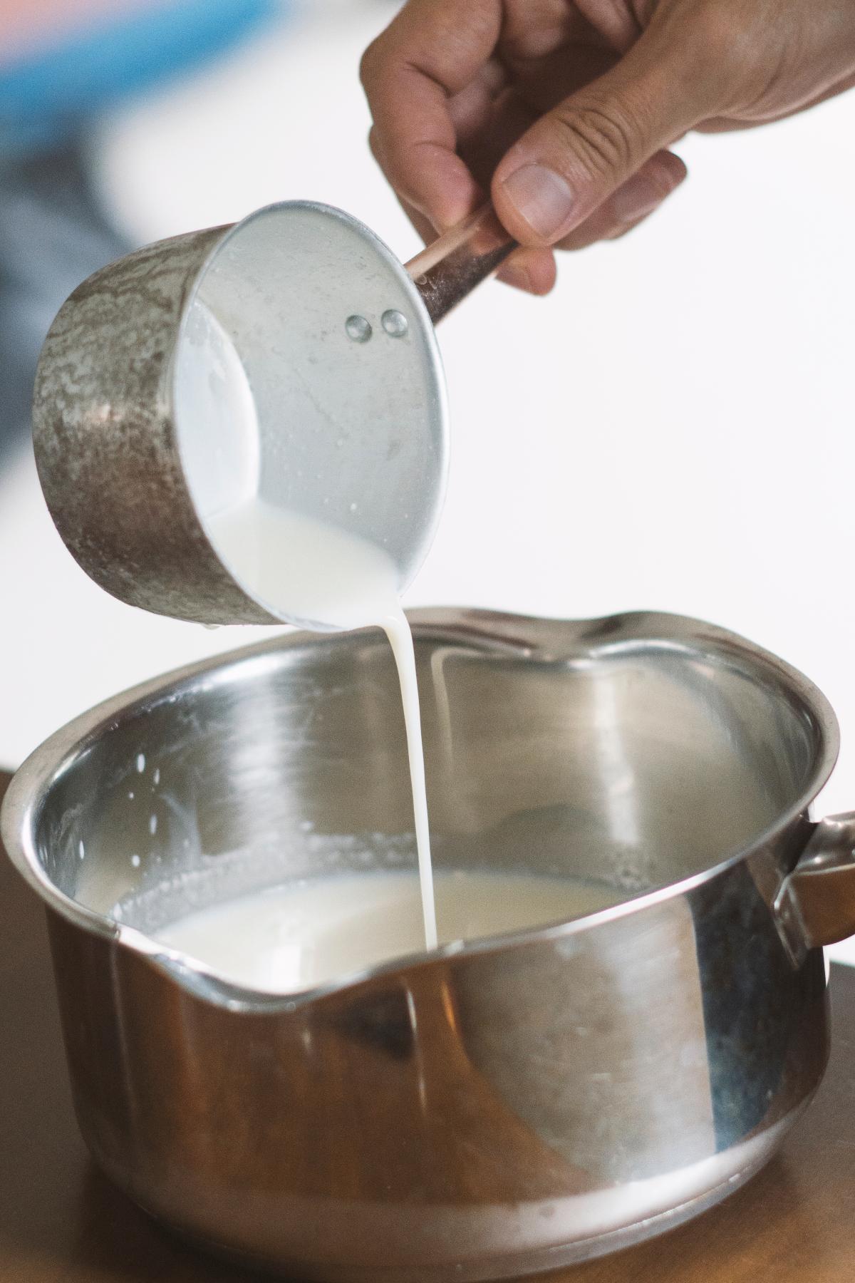Mano che versa il latte nel pentolino