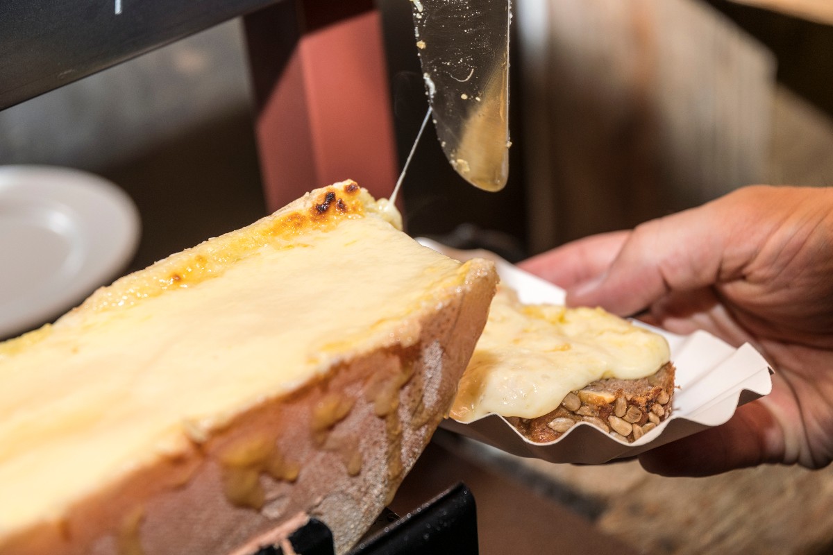 Raclette con formaggio che si scioglie e viene versato su una fetta di pane.