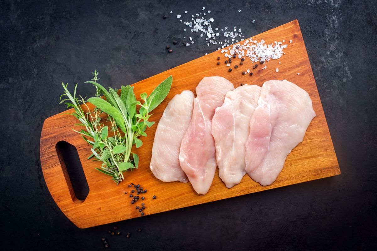 Vista dall'alto bistecche crude su tagliere di legno con erbe aromatiche, sale e pepe