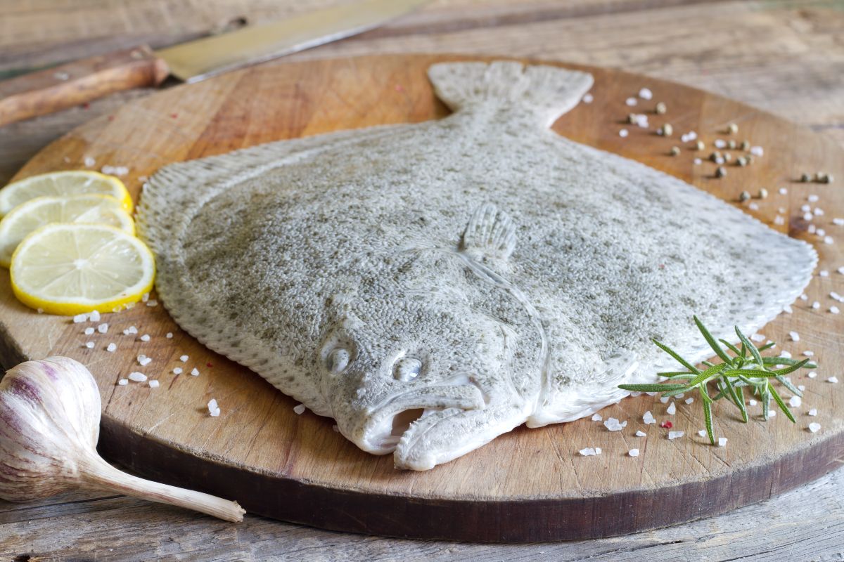 Pesce rombo su tagliere di legno con vicino aglio e limone