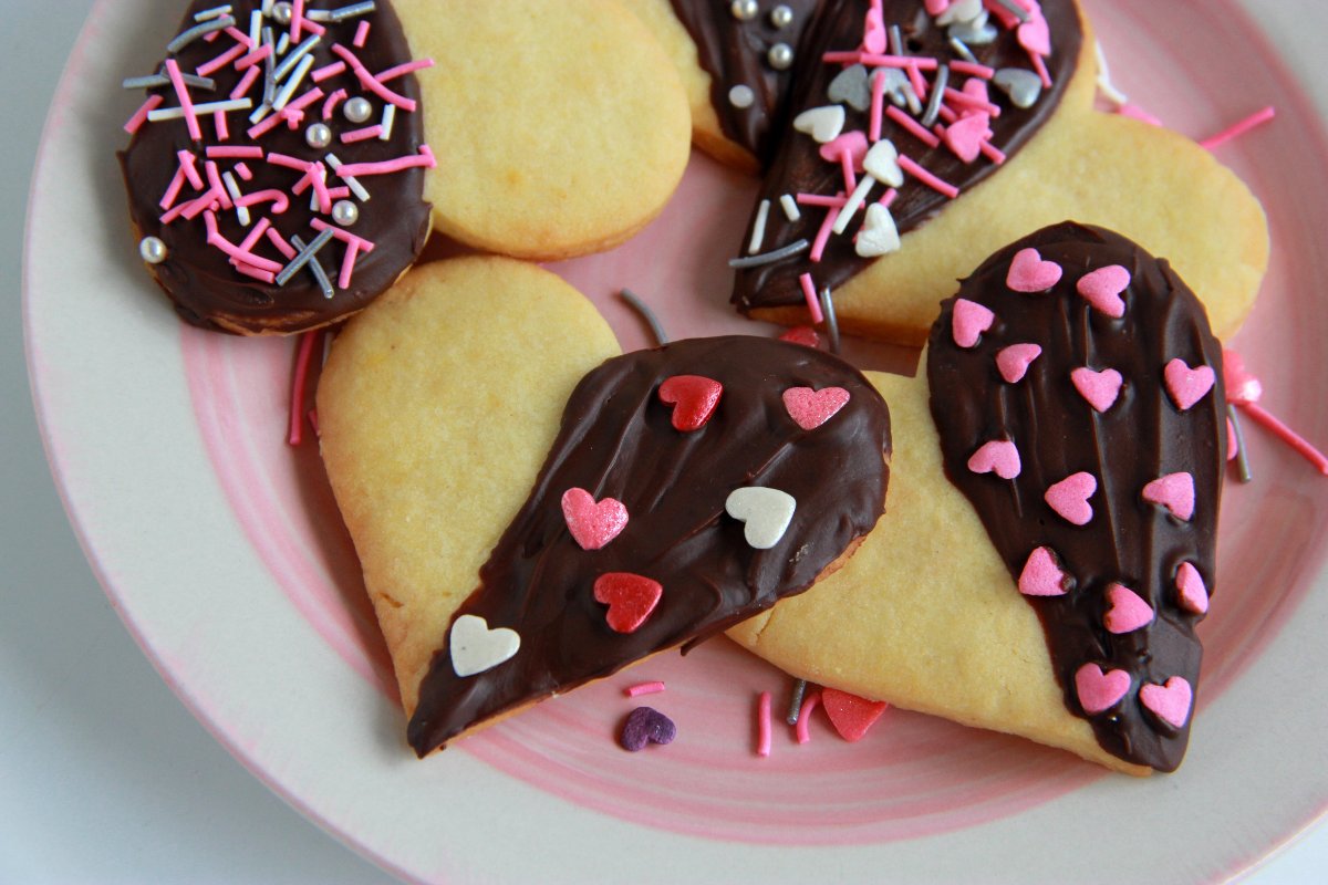 Biscotti di pasta frolla a forma di cuore ricoperti per metà con cioccolato e decorati con zuccherini 