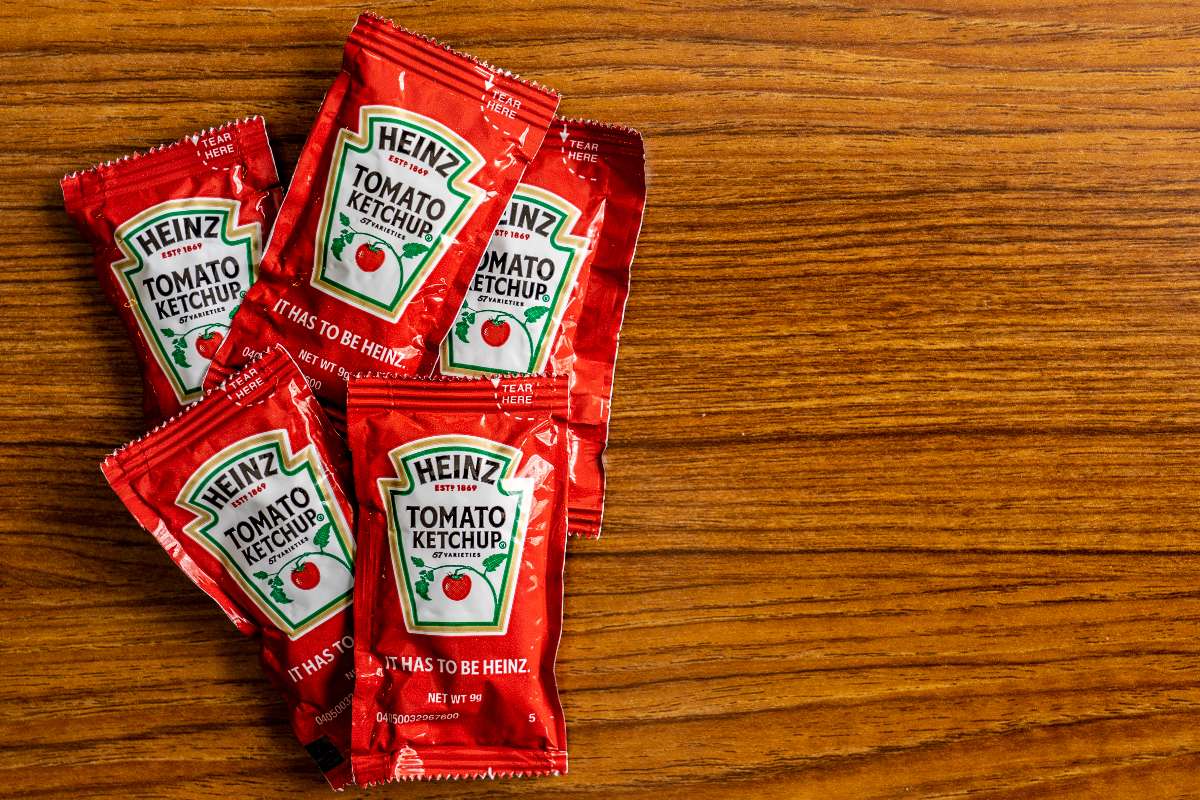 Bustine di ketchup distribuite su una superficie di legno.