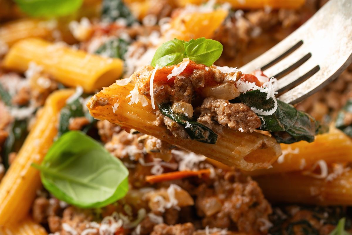 Forchetta con pasta tipo penne condite con ragù e spinaci