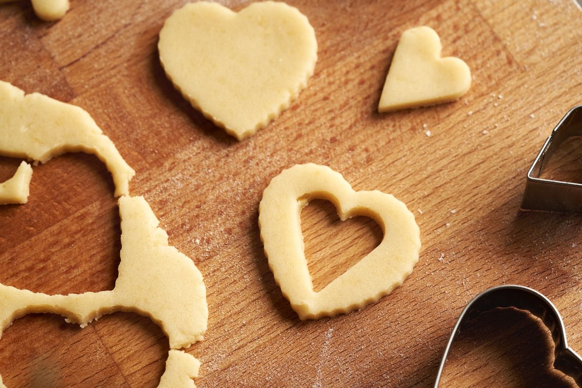 Vista dall'alto tagliere di legno con biscotti di pasta frolla a forma di cuore con finestra a cuore ancora da cuocere