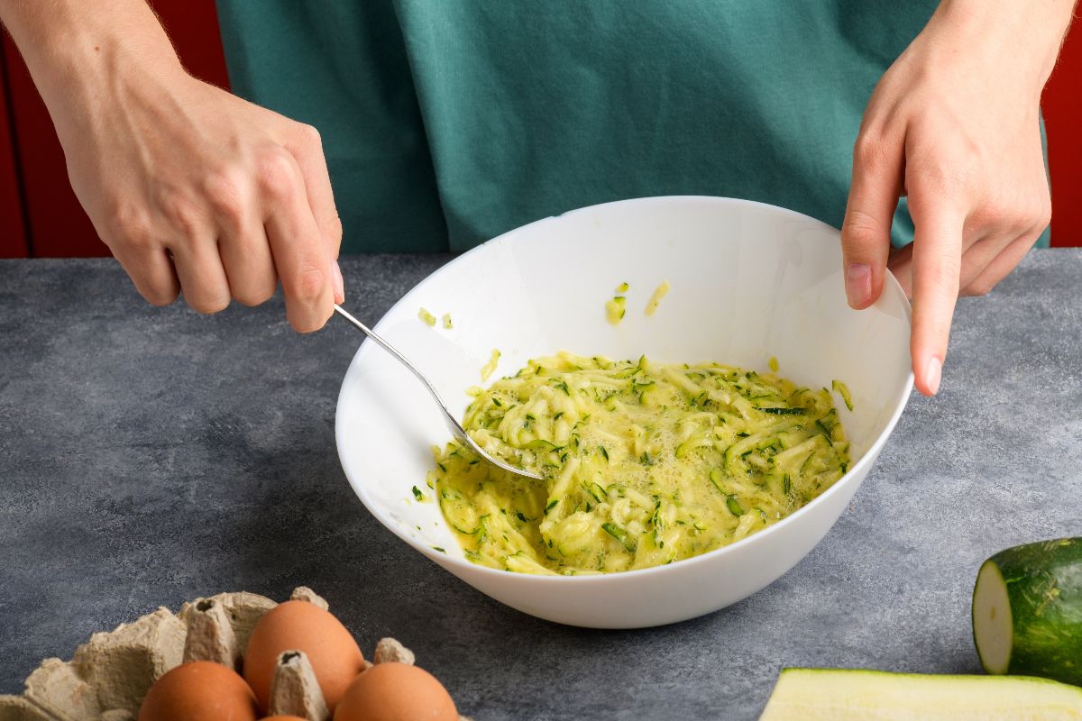 Mani di donna che mescolano uova con zucchine grattugiate per preparare frittata