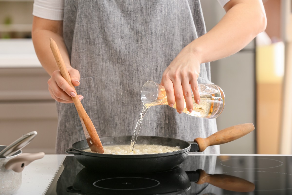 Donna che prepara il risotto aggiungendo il vino bianco in padella