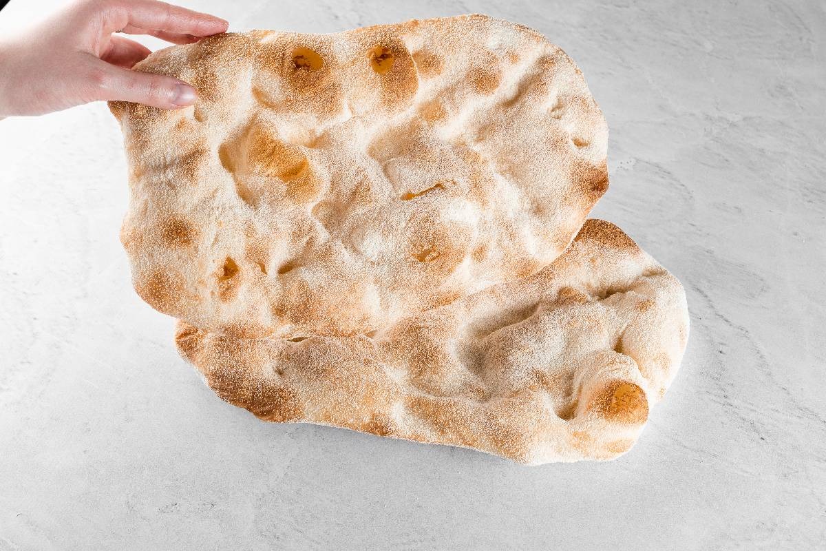 Mano femminile che mostra una base precotta per pinsa romana