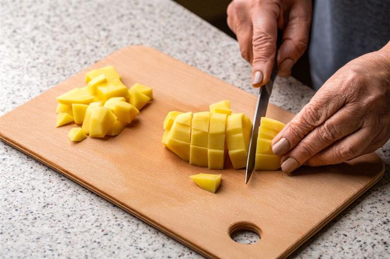 Mani di donna che tagliano patate a cubetti su tagliere di legno