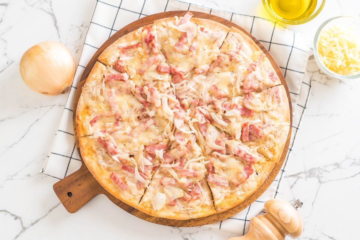 Vista dall'alto pizza con panna, cipolle e speck su tagliere di legno