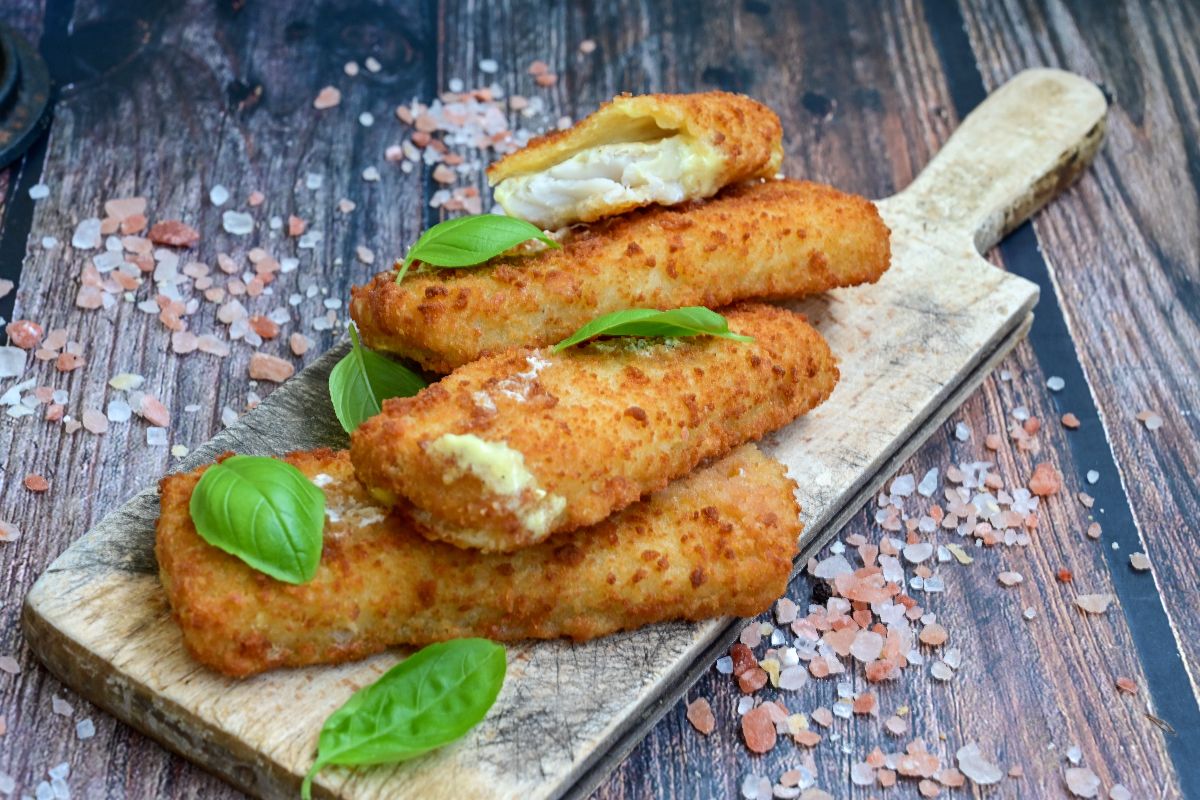 Le cotolette di merluzzo impanate disposte su un tagliere di legno.