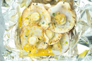 Vista dall'alto capesante su foglio di allumino con prezzemolo, scorza di limone e burro