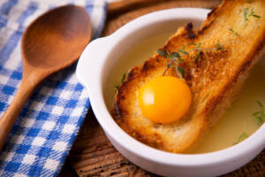 Terrina bianca con brodo, fetta di pane e uovo crudo