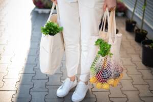 Donna che porta due borse della spesa con frutta e verdura