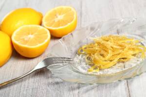 Scorze di limoni tagliate a bastoncini e candite su piatto di vetro trasparente con limoni sullo sfondo